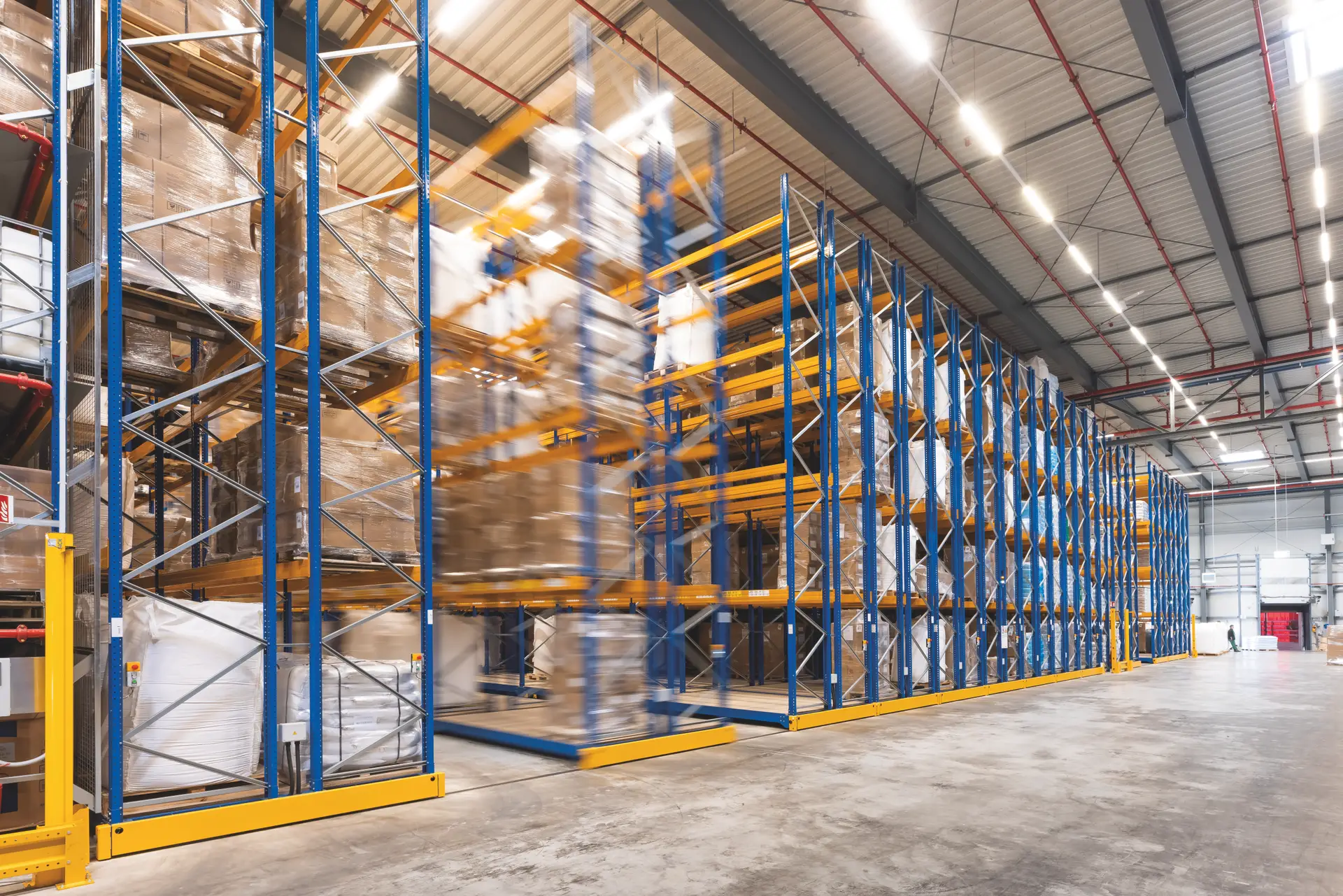 מבט קרוב על מסילות מתכת בתחתית מדף נייד שנע בתוך מסילה במשטח הבטון של המחסן