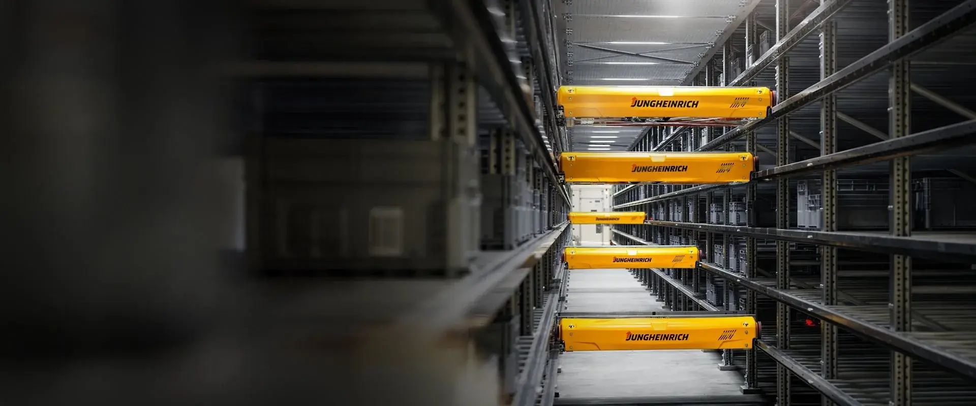 מבט אווירי על מספר שאטלים צהובים של מערך Miniload Shuttle פועלים במקביל במדפי אחסון צרי-פס, לטיפול במכולות קטנות