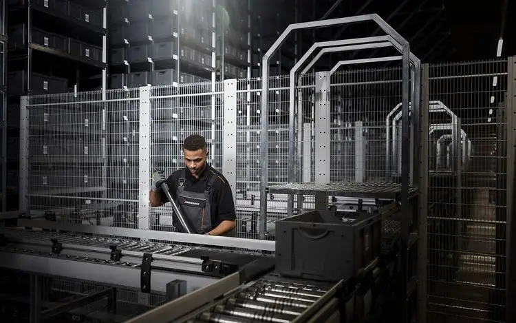 עובד מוסיף מכל פלסטיק לבניית זרם השינוע על מסוע תוף במערכת שינוע למכלי פלסטיק