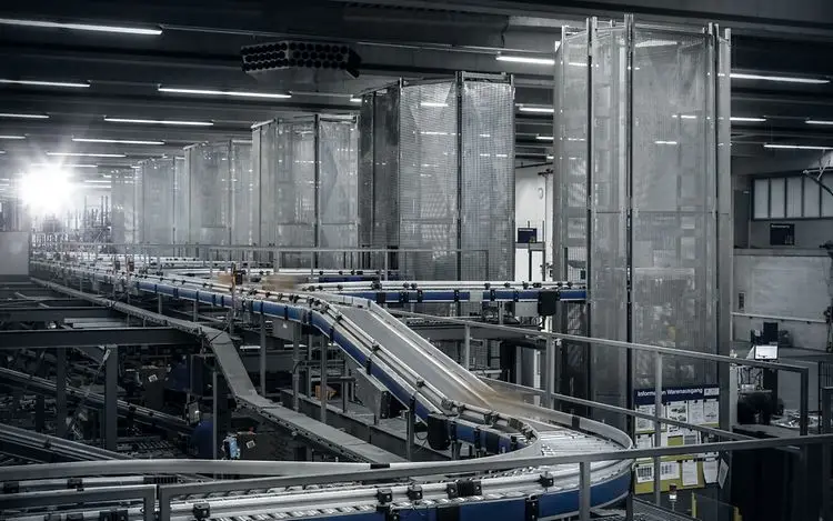 מבט כללי על מערכת מסוע מורכבת בחלל מפעל, משנעת מכלי פלסטיק בכיוון רציף