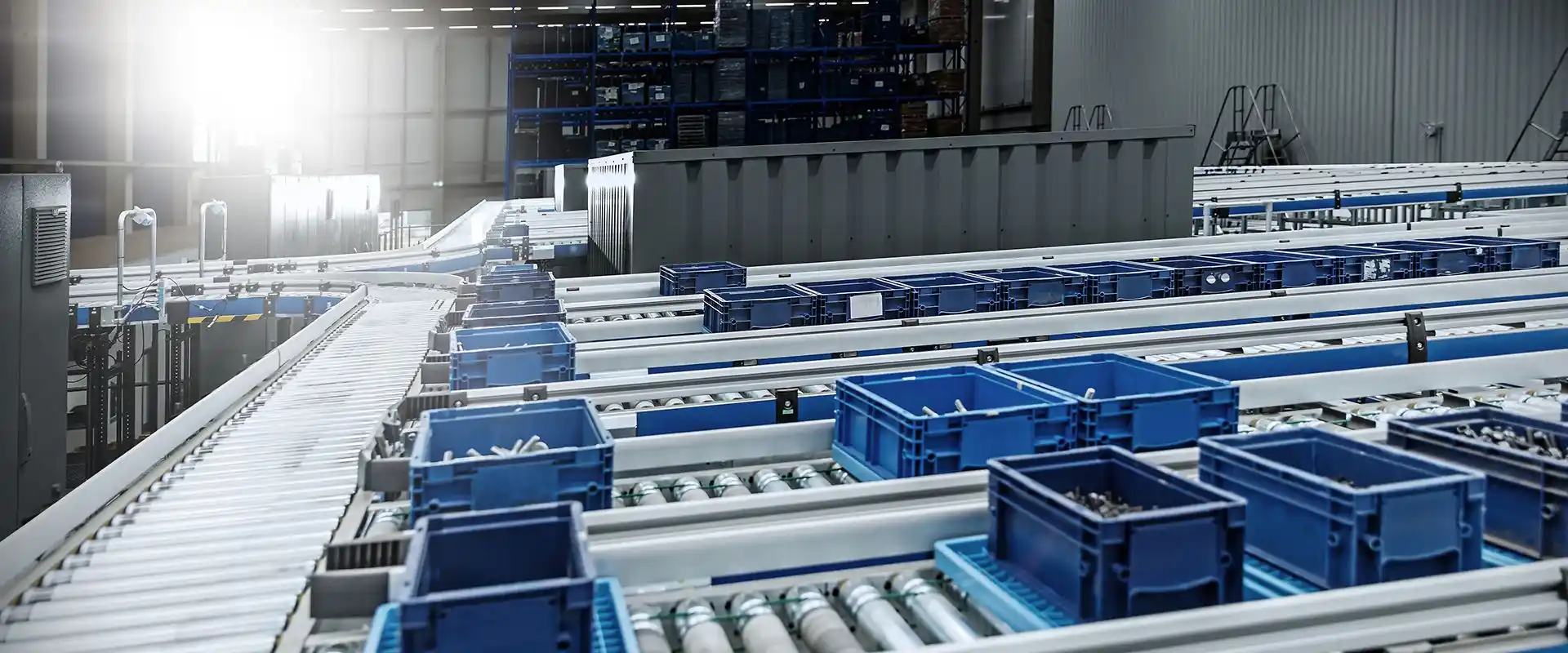 מבט ממעוף הציפור על רצף מסועי גלילים ומסועי רצועה בשילוב מכלי פלסטיק כחולים, במערכת שינוע אוטומטי למחסנים