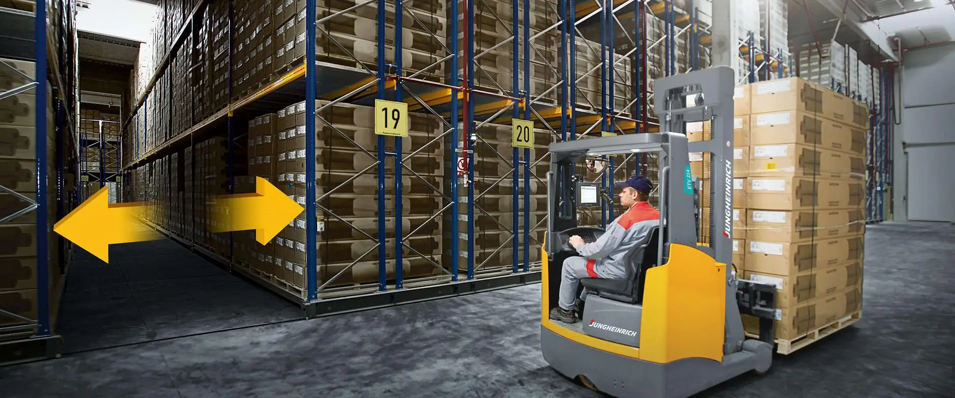 מלגזה עומדת מול שורה של מדפים ניידים תעשייתיים גדולים במפעל, כשחץ דו־כיווני מסמן את אפשרות התנועה