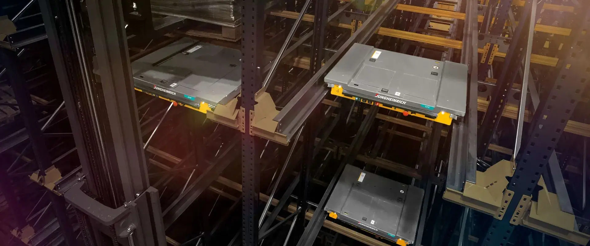 מבט על מדפים קומפקטיים עם מסילות רוחביות ושאטלים צהובים שנעים לאורך התעלות, בחלל מחסן תעשייתי